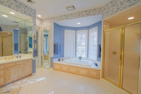 A spacious primary bathroom from the 1980s featuring a large, oval whirlpool bathtub dropped into a tiled platform.